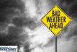 An image of dark, stormy clouds with a bold yellow weather warning sign.