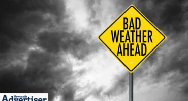 An image of dark, stormy clouds with a bold yellow weather warning sign.