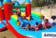 A photogragh of a group of small children having fun on a red, blue, green and yellow water slide inflatable.