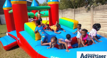 A photogragh of a group of small children having fun on a red, blue, green and yellow water slide inflatable.