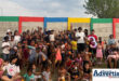 A group photo of a large crowd of people and children photographed in front of a colourful wall.