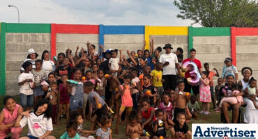 A group photo of a large crowd of people and children photographed in front of a colourful wall.