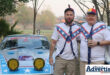 Two people dressed up are photographed standing in front of a vintage car.