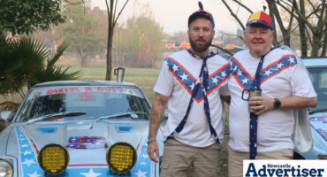 Two people dressed up are photographed standing in front of a vintage car.