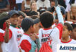 A photo of a group of kids, smiling while wearing white and red KFC Mini Cricket Tshirts and backpacks.