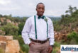 A photo of a young gentlemen dressed in fancy attire standing outside in a field with rocks.