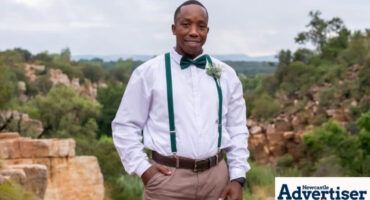 A photo of a young gentlemen dressed in fancy attire standing outside in a field with rocks.