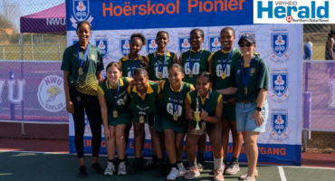 Netball players standing in front of Hoërskool Pionier's banner.