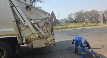 Image of a municipal dump truck with a worker picking up litter.