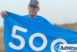 A parkrunner is photographed holding a 500 milestone banner during a run.