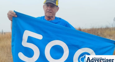 A parkrunner is photographed holding a 500 milestone banner during a run.