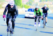 Image of three cyclists, one in the foreground, in helmets racing on a road.