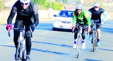 Image of three cyclists, one in the foreground, in helmets racing on a road.