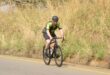 Photo of a cyclist on a road next to a field.