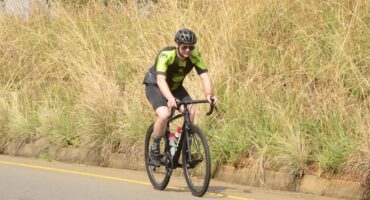 Photo of a cyclist on a road next to a field.