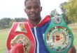 Image of a boxer wearing gloves and his championship belts.