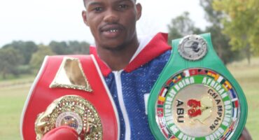 Image of a boxer wearing gloves and his championship belts.