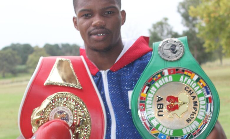 Image of a boxer wearing gloves and his championship belts.