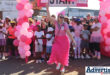 A woman completely dressed in pink poses in front of a large group of people dressed in pink during a fun run in Newcastle.