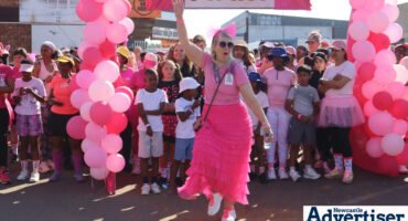 A woman completely dressed in pink poses in front of a large group of people dressed in pink during a fun run in Newcastle.