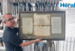 Image of a man who holds framed 1895 documents.