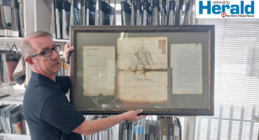 Image of a man who holds framed 1895 documents.