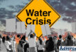 A large background image of a colourful sky with a yellow board saying 'Water Crisis' in bold black text. In the forefront is a group of people busy protesting.