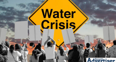 A large background image of a colourful sky with a yellow board saying 'Water Crisis' in bold black text. In the forefront is a group of people busy protesting.