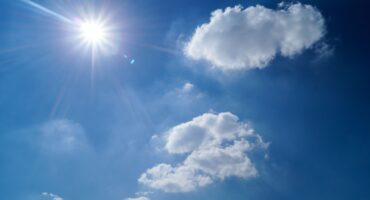 Image of the sun in the sky with a few clouds.