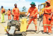 Image of workers in orange overalls with a machine fixing potholes.