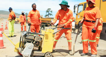 Image of workers in orange overalls with a machine fixing potholes.