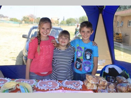 Marizelle Pretorius (10), Louize Stoltz (6) en Nathan Pretorius (9) beman vir 'n oomblik die stalletjie met handgebreide klere vir babas en ander produkte.