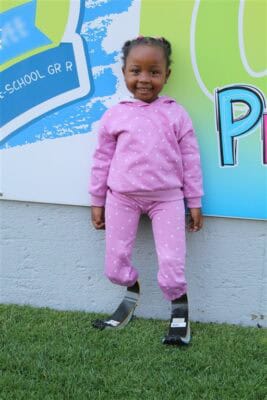 Leano Langa in a pink tracksuit stands against a wall, showing her prosthetic legs.