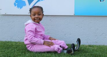 Leano Langa sits on grass in a pink tracksuit showcasing her prosthetics