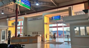 The sunlit, open interior of the Polokwane International Airport terminal building, showing the check-in counter, information signage for arrivals/departures and parking, and a glass entrance leading outside.