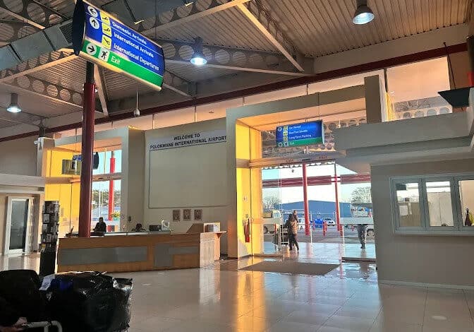 The sunlit, open interior of the Polokwane International Airport terminal building, showing the check-in counter, information signage for arrivals/departures and parking, and a glass entrance leading outside.