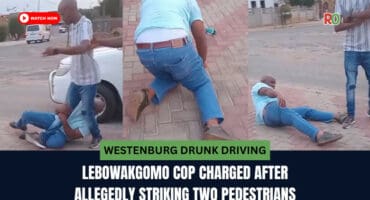 A man in jeans and a light blue shirt lies on a paved surface while another man stands nearby, appearing to restrain him.