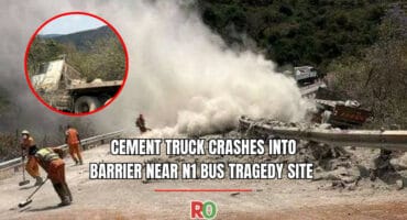 A news graphic reporting a truck crash near the N1 bus tragedy site. The main image shows emergency workers in white dust and debris, cleaning a road where a guardrail is destroyed. An inset shows the wrecked white truck on a steep slope. The text reads: "CEMENT TRUCK CRASHES INTO BARRIER NEAR N1 BUS TRAGEDY SITE."