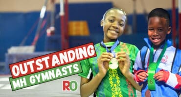 Two Mitchell House gymnasts show off their medals with a gymnastics studio in the background.