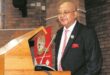 Photograph of Judge President George Phatudi, a bald, light-skinned man wearing glasses, a black pinstripe suit, and a red and white striped tie, standing behind a wooden podium and speaking into a microphone.