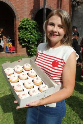 A woman holds a box of cupcakes.