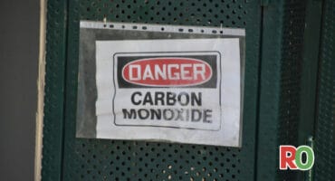 a plastic sleeve with a danger warning placed inside, it says Danger Carbon Monoxide, the plastic sleeve is ziptied to a green metal gate