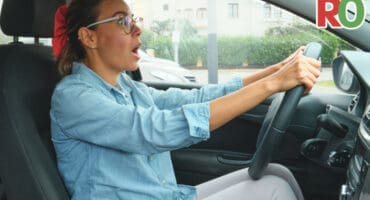 Woman driving in car, looking surprised.