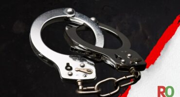 Pair of silver metal handcuffs against a dark, textured surface.
