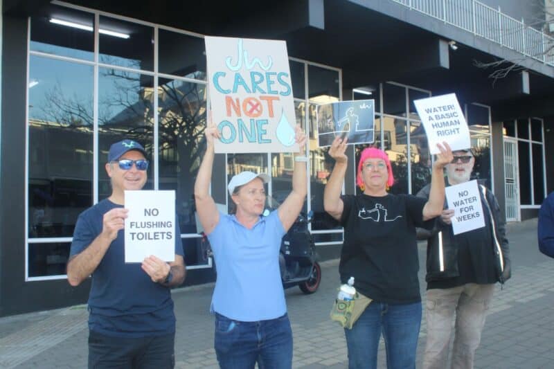 As trickles of water return to parts of Melville, frustrated residents protest ongoing supply failures while one Westdene pensioner finds relief and laughter, under a rain shower.