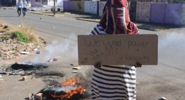 Italian Road resident holds a placard showing her frustrations over the three-month power outage on August 3, 2026, in Newlands. Photo: Waydon Jacobs