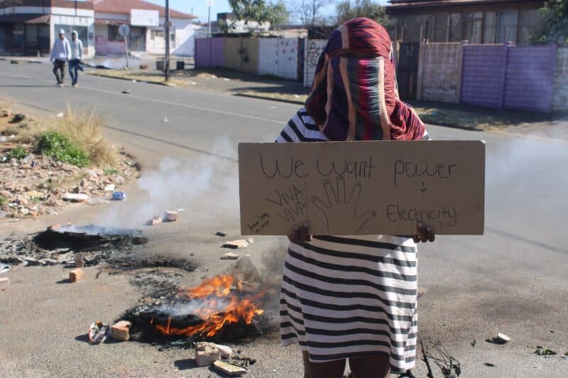 Italian Road resident holds a placard showing her frustrations over the three-month power outage on August 3, 2026, in Newlands. Photo: Waydon Jacobs