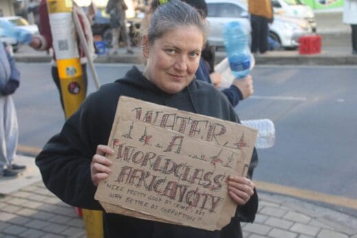 Melville resident Kirsty Jurgens holds a placard reading "Water, a mordiculous archaicity" during the water protest in Melville on August 14, 2026, on Main Road. Photo: Waydon Jacobs