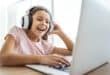 Smiling young girl wearing headphones while participating in an online lesson on a laptop.