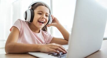 Smiling young girl wearing headphones while participating in an online lesson on a laptop.